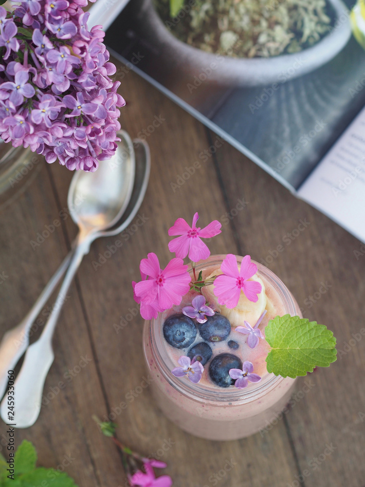 Glass of smoothie with blueberries and banana. Blossoming lilac flowers with magazine on wooden table. Glass of smoothie with blueberries and banana. Blossoming lilac flowers with magazine on wooden table.