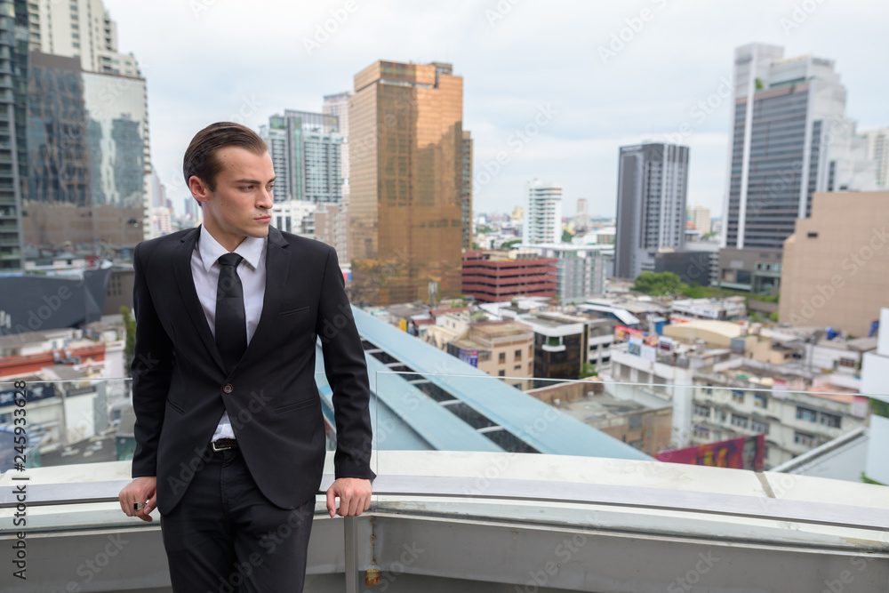 Young businessman thinking outdoors in city with rooftop view Young businessman thinking outdoors in city with rooftop view