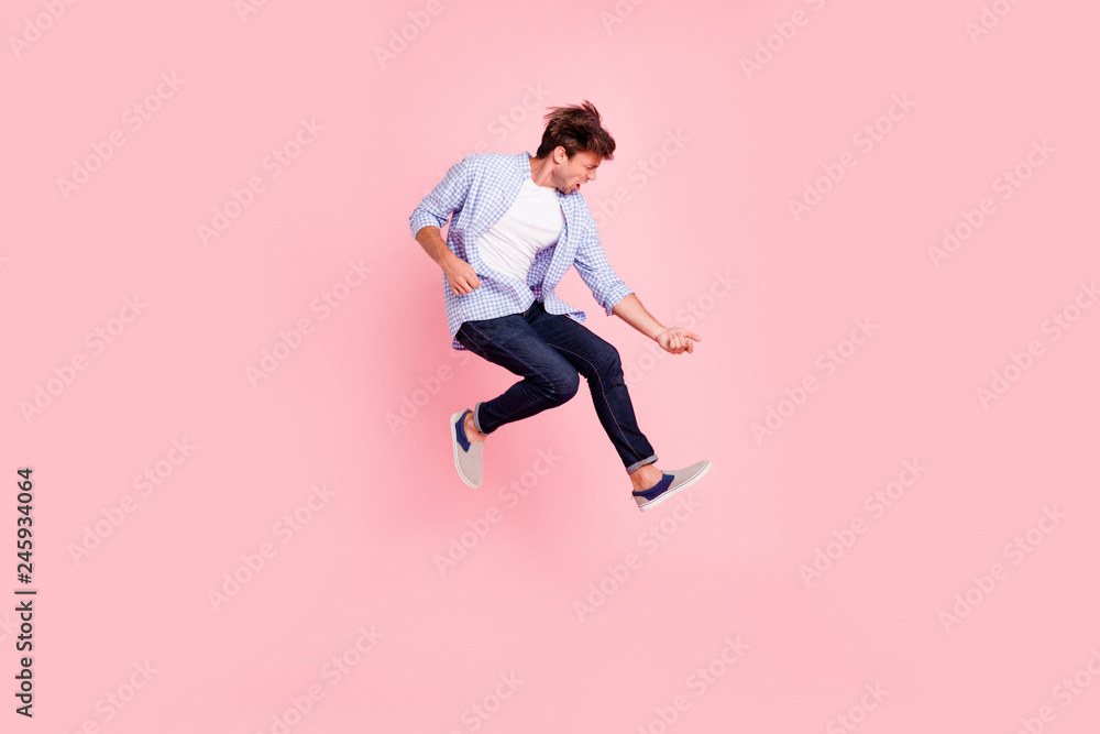 Full length body size photo of jumping high crazy he his him handsome playing imagine electric guitar in arms hands harsh face wearing casual jeans checkered plaid shirt isolated on rose background