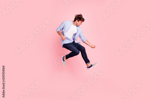 Full length body size photo of jumping high crazy he his him handsome playing imagine electric guitar in arms hands harsh face wearing casual jeans checkered plaid shirt isolated on rose background