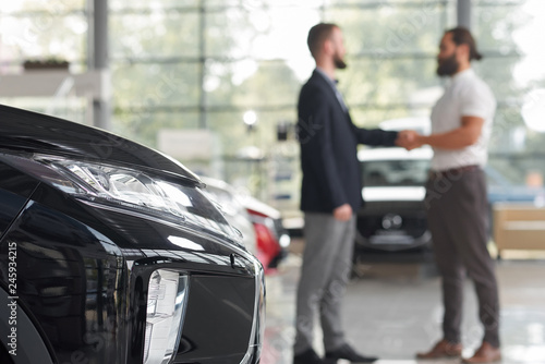 Car dealer shaking hands with client in car showroom. © serhiibobyk