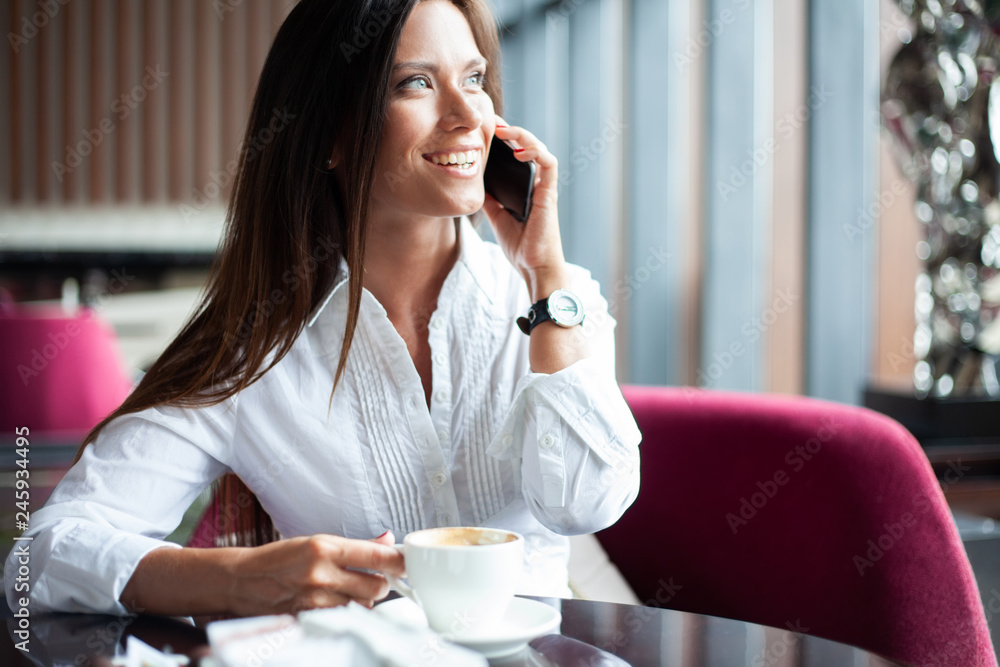 Young charming woman calling with smartphone while sitting alone in coffee shop during free time, attractive female with cute smile having talking conversation with mobile phone while rest in cafe. Young charming woman calling with smartphone while sitting alone in coffee shop during free time, attractive female with cute smile having talking conversation with mobile phone while rest in cafe.