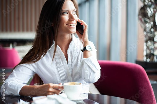 Young charming woman calling with smartphone while sitting alone in coffee shop during free time  attractive female with cute smile having talking conversation with mobile phone while rest in cafe.