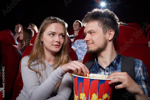 Young couple eating popcorn looking each other.
