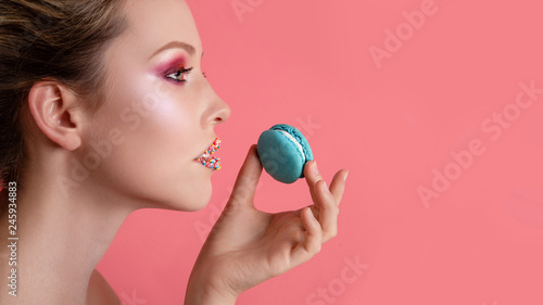Beauty fashion model girl with colourful makeup taking blue macaron. Beautiful woman, bright make-up. Diet,dieting concept. Sweets. Closeup
