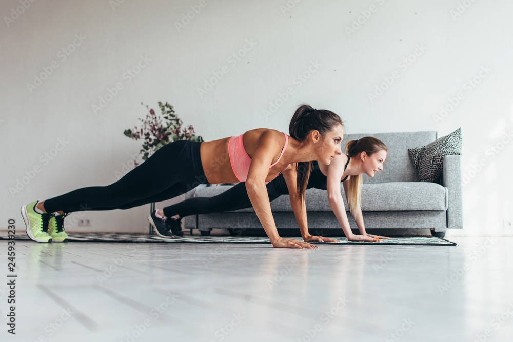 Obraz premium Two fitness women doing push-ups exercise working out at home. Side view