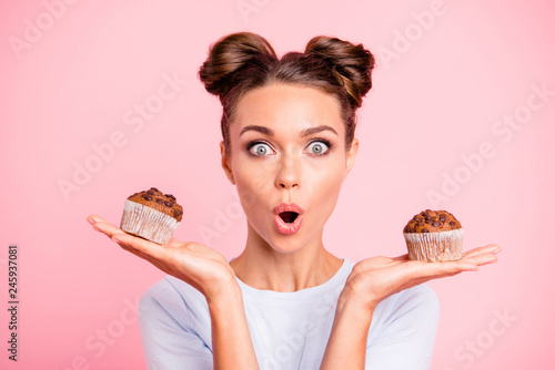 Close-up portrait of nice lovely cute attractive amazed scared afraid girl holding in hands two cakes choosing deciding dilemma opened mouth isolated over pink pastel background