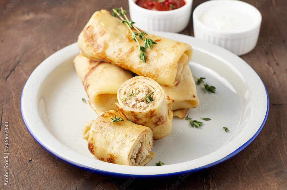 Savory crepe rolls with ground meat filling served with sour cream and tomato sauce Savory crepe rolls with ground meat filling served with sour cream and tomato sauce