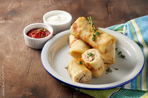 Savory crepe rolls with ground meat filling served with sour cream and tomato sauce
