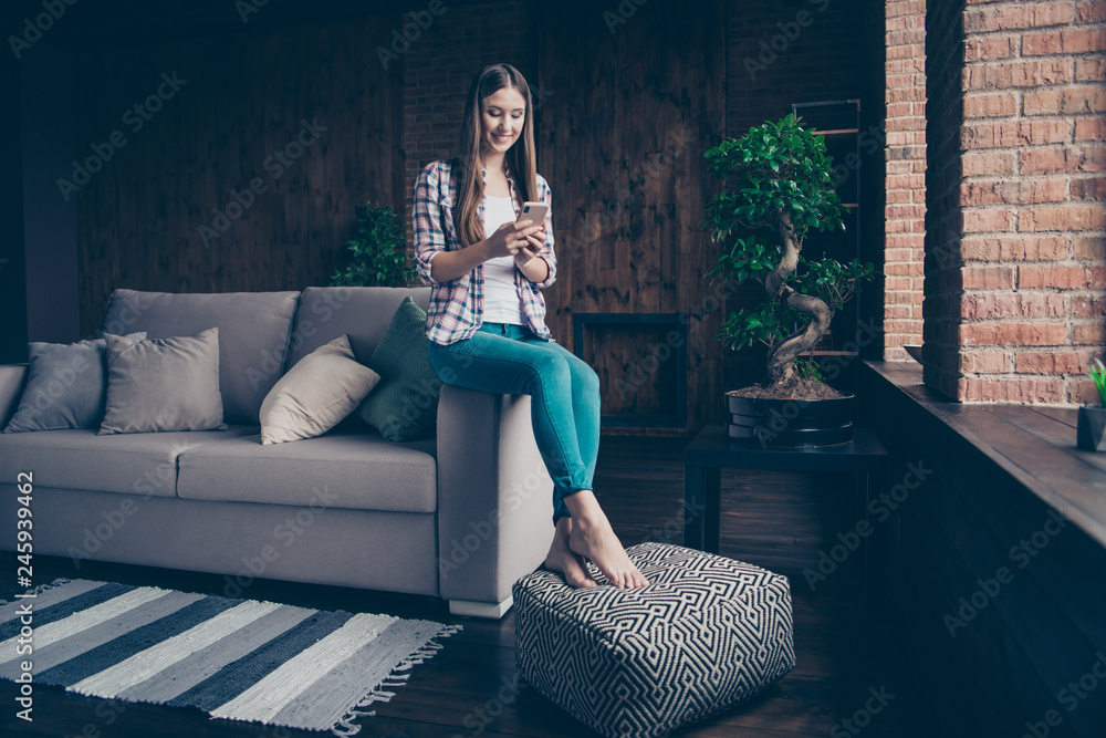 Obraz premium Full length body size photo portrait of cheerful positive concentrated cute nice glad slim fit she her girl student sitting on divan pouffes using telephone smartphone