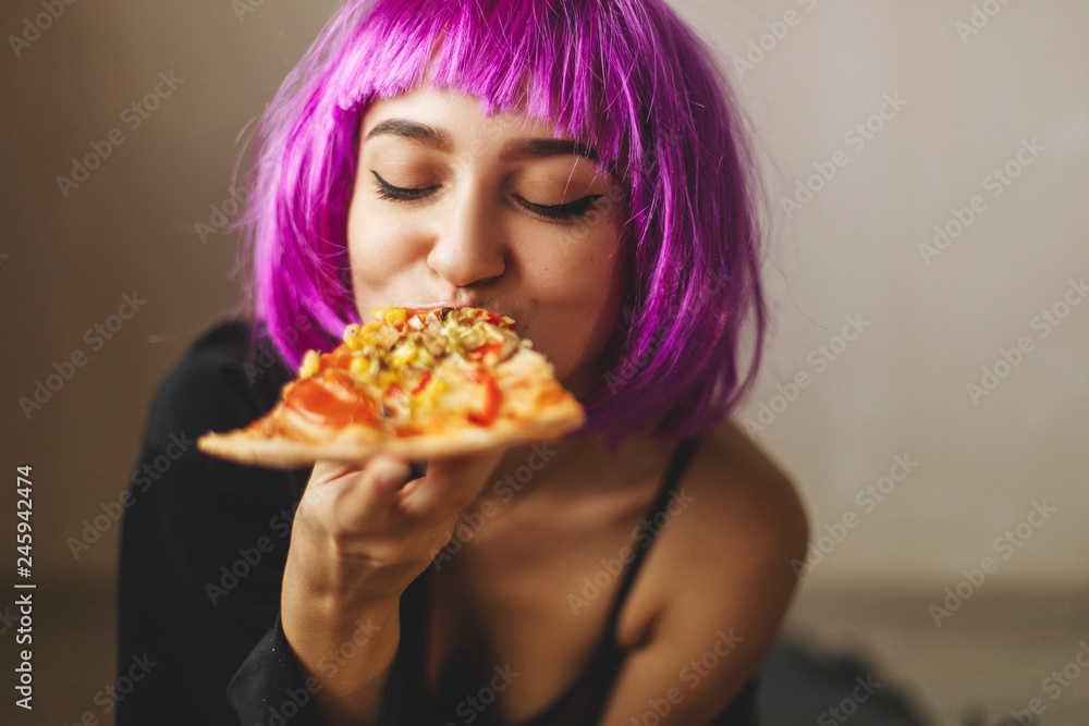 Funny pink hair wig girl in black lingerie and shirt eating pizza at home. Girl enjoying a delicious pizza. Funny pink hair wig girl in black lingerie and shirt eating pizza at home. Girl enjoying a delicious pizza.