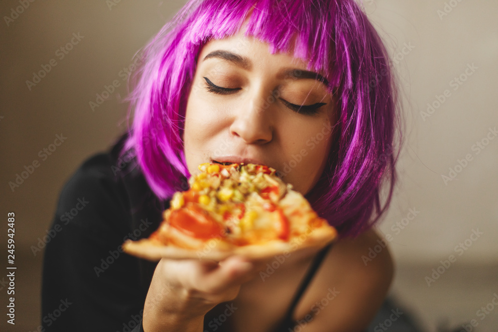 Funny pink hair wig girl in black lingerie and shirt eating pizza at home. Girl enjoying a delicious pizza. 