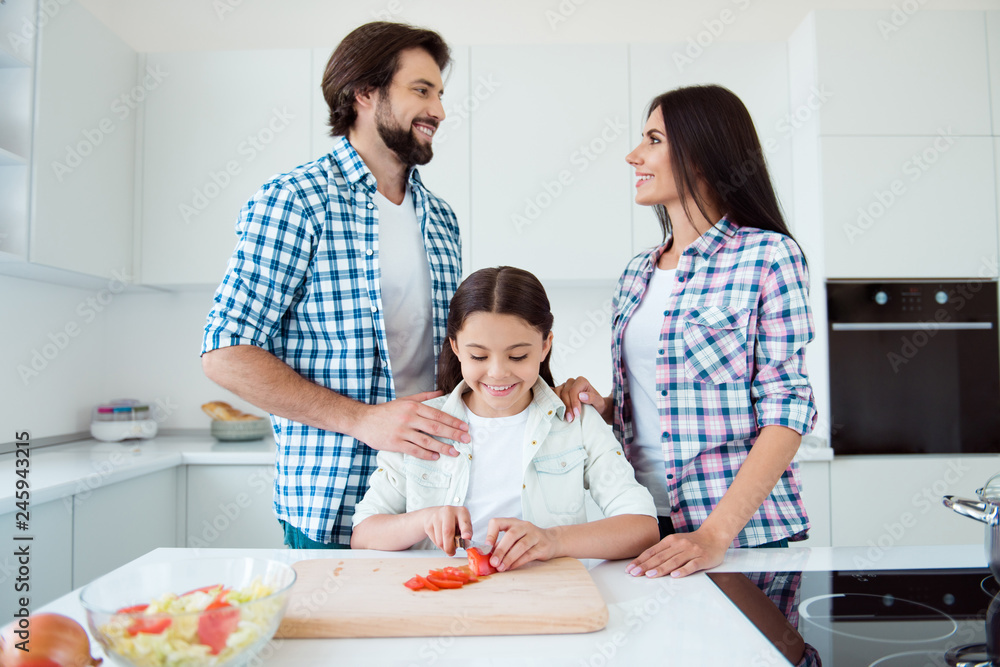Portrait of nice lovely tender sweet attractive cheerful cheery kind people mom dad helping pre-teen kid making fresh salad dish on board in light white interior room Portrait of nice lovely tender sweet attractive cheerful cheery kind people mom dad helping pre-teen kid making fresh salad dish on board in light white interior room