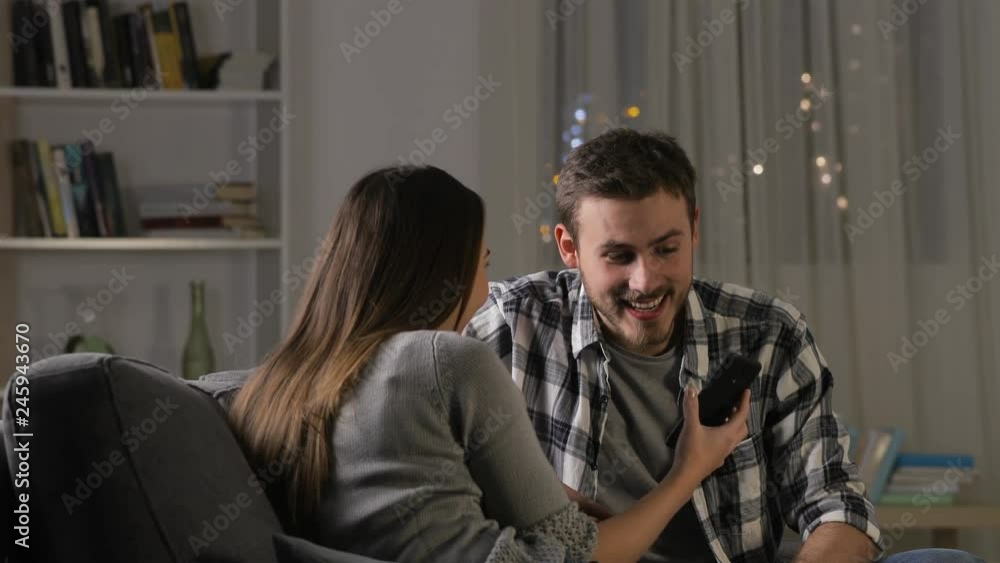 Two happy friends giving high five checking smart phone content in the night sitting on a couch at home Two happy friends giving high five checking smart phone content in the night sitting on a couch at home