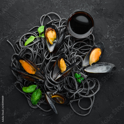 Black pasta with mussels on a black stone background. Top view. Free space for your text.