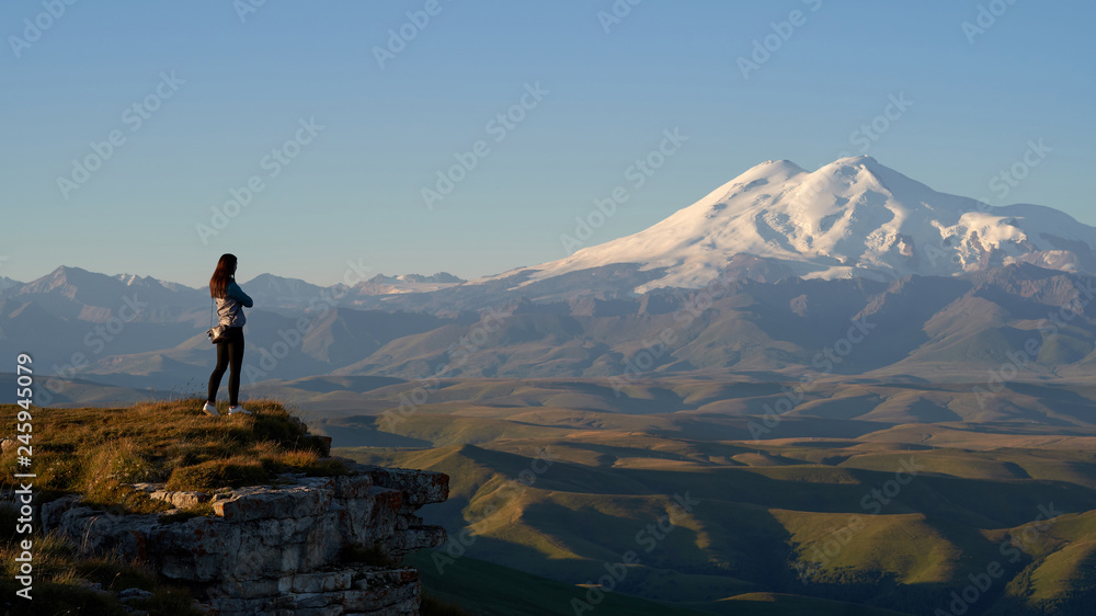 Woman traveller, Mount Elbrus and Bermamyt Plateau in the background at sunrise. Caucasus mountains, Russia. 
