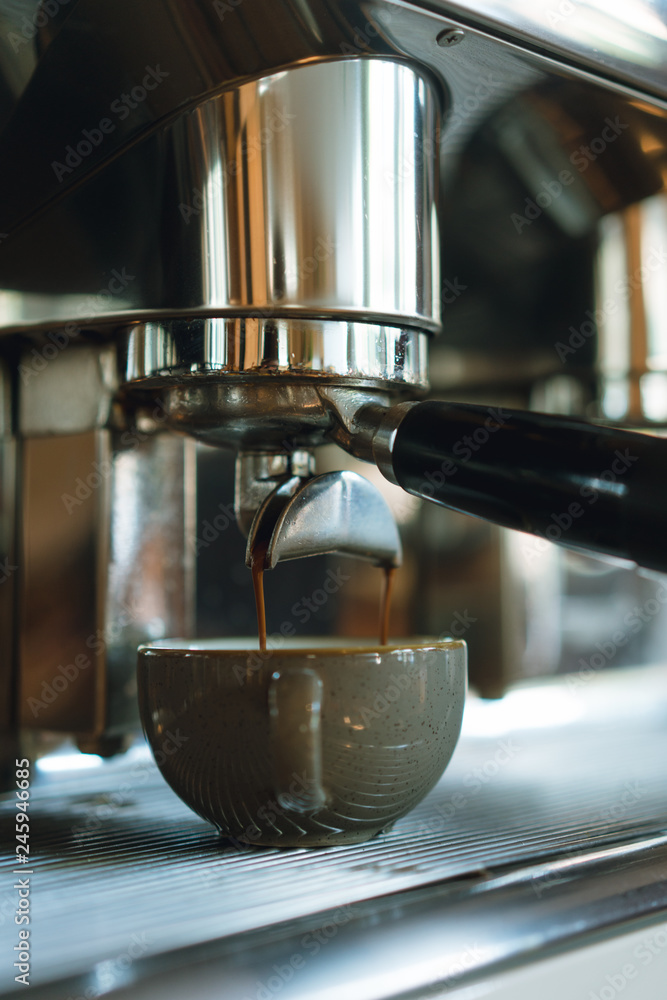Hot coffee streaming from a coffee machine into a ceramic grey cup in a bar, barista making latte using professional equipment Hot coffee streaming from a coffee machine into a ceramic grey cup in a bar, barista making latte using professional equipment