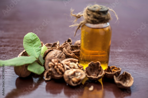 Close up of herbal organic extracted walnut oil in a transparent glass bottle with raw wall nuts on wooden surface. photo