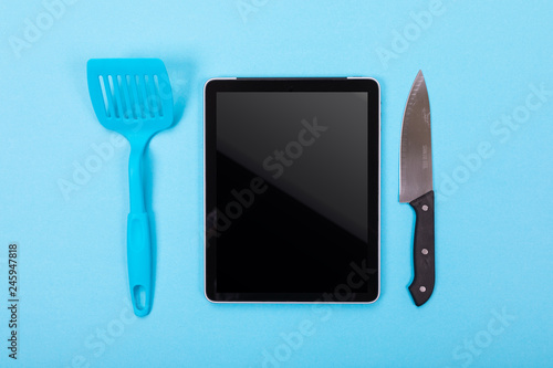 top view of the tablet and kitchen utensils next to it isolated on a blue background