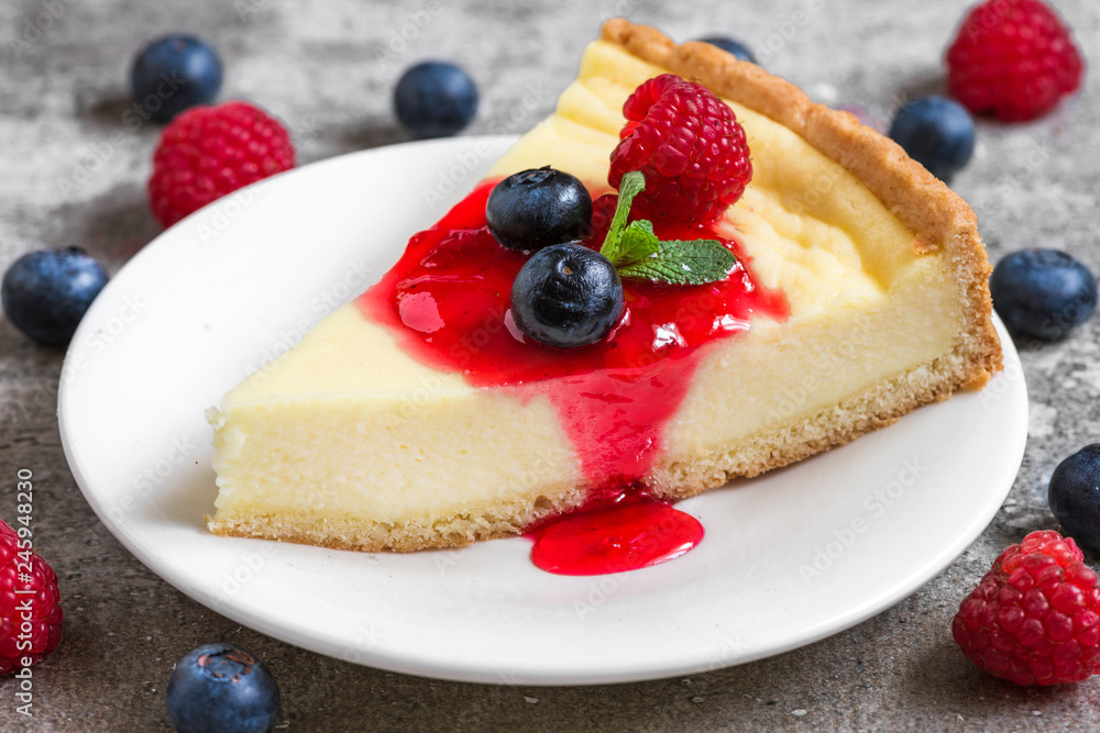 slice of cheesecake with fresh raspberries, blueberries, jam and mint on concrete background. close up slice of cheesecake with fresh raspberries, blueberries, jam and mint on concrete background. close up