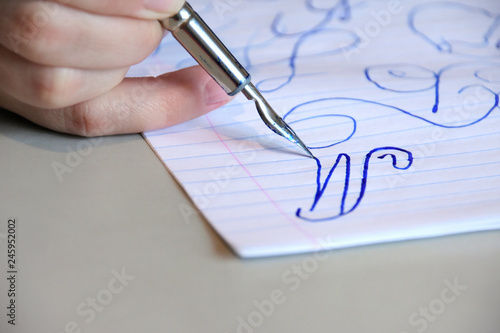 White woman hand with steel nib pen writing on sheet of paper. Handwriting classic calligraphy elements by blue ink and old vintage pen. Drawing design signature with beautiful letter. Lettering