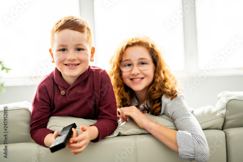 Happy girl and boy watching tv with remote control