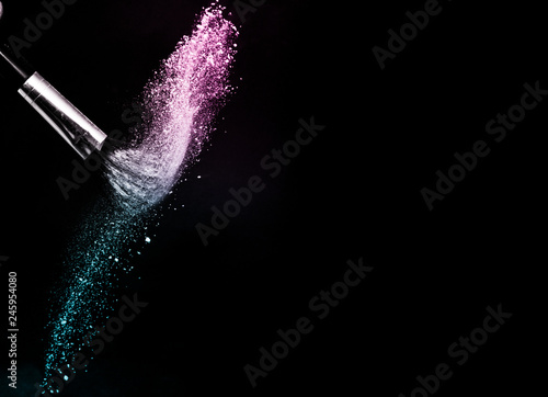 Cosmetic brush with purple and blue ocean cosmetic powder spreading for makeup artist or graphic design in black background