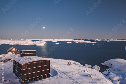 Antarctic research Vernadsky station buildings next to the Antarctica shoreline. Stunning winter landscape. The snow covered land surrounded by the frozen ocean. The harsh environment. Night scene