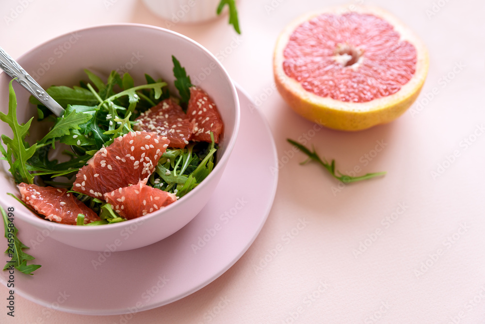 Fresh citrus salad with arugula, grapefruit and sesame seeds on pink background. Selective  focus. Raw vegetarian spring detox food.