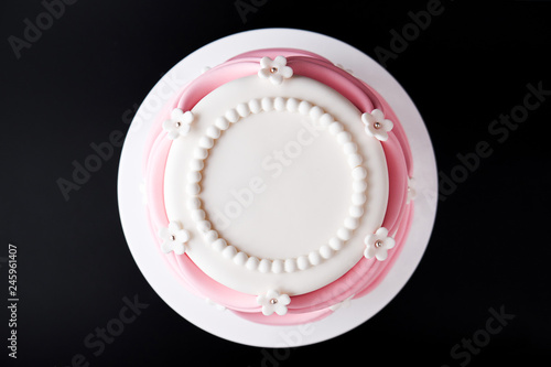 White wedding cake with pink elements made from pastry mastic on a black background. Top view. Sugar flowers, marzipan flowers and mastic, beautiful decor for decorating cakes. Close-up.