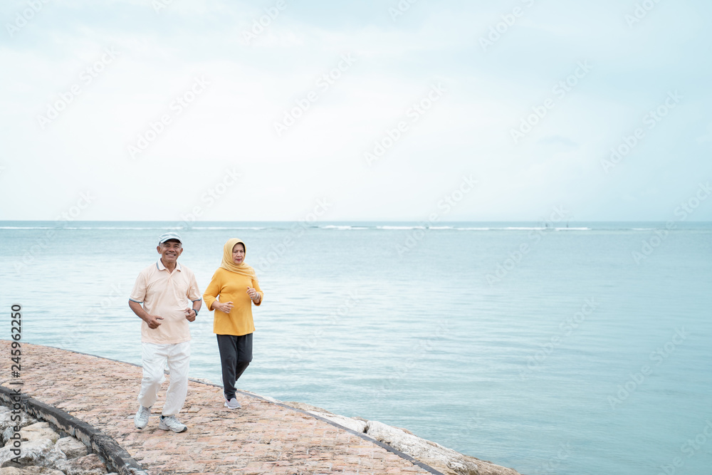 senior man and woman together running on the beach