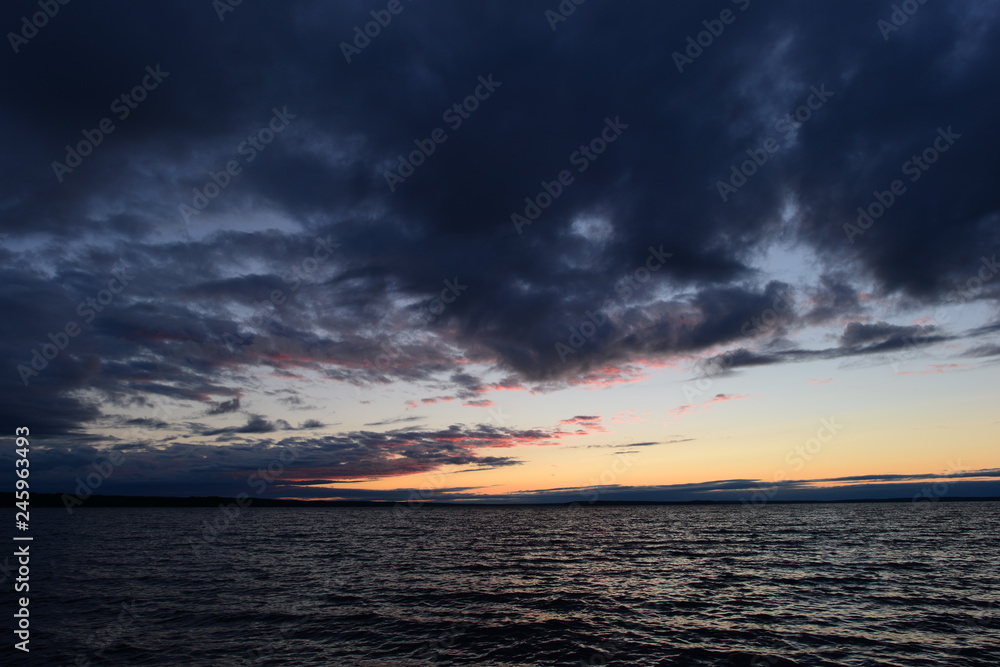 Night sky with twilight glow in the clouds above the dark waves of the lake water. Night sky with twilight glow in the clouds above the dark waves of the lake water.