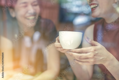 Two Asian women,friends having a free time drinking coffee at cafe. Friends laughing together while drinking a coffee in the restaurant, photo from outside the window.