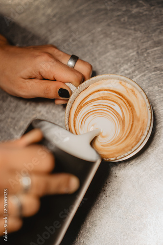 Professional barista pouring steamed milk into coffee cup making beautiful latte art pattern, female hands crop view, latte art by bartender,