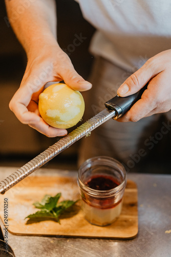 close up image of male hands cookind desert. the chef is rubbing grated lemon to decorate the pudding. Concept of restaurant kitchen
