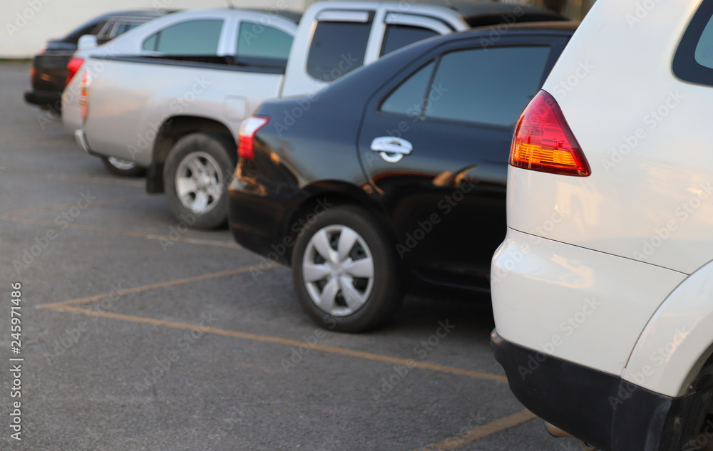 Closeup of back or rear side of white car and other cars parking in parking area with natural background in twilight evening of sunny day. 