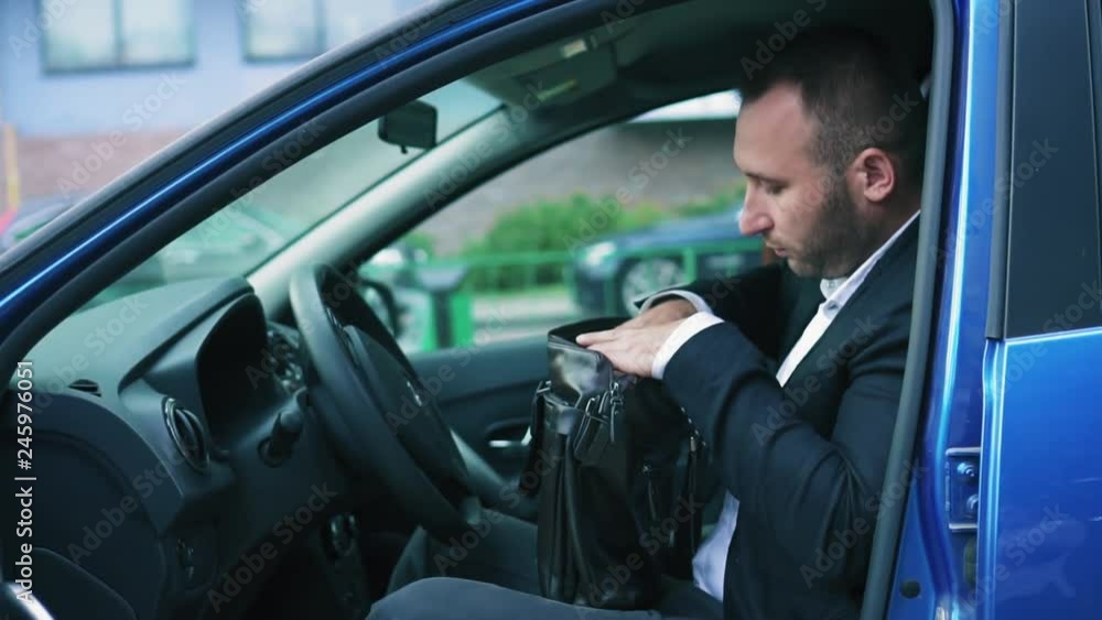 Businessman sitting in the car, opened his briefcase and sorting through the documents. Suddenly he finds a strange item in his bag and is surprised at this Businessman sitting in the car, opened his briefcase and sorting through the documents. Suddenly he finds a strange item in his bag and is surprised at this