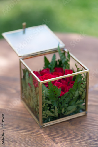 glass box with red flowers and greenery for wedding rings