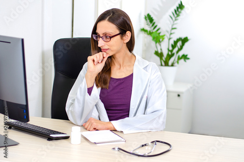 Young woman doctor with glasses doing research at her desk © eshana_blue