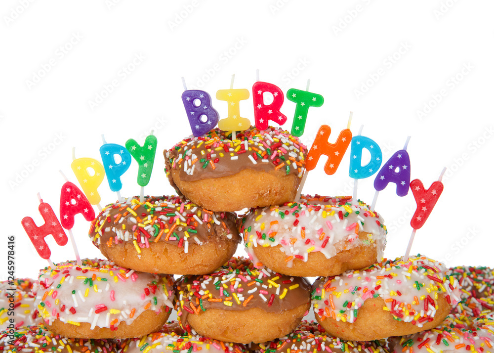 Chocolate and white frosted donuts covered in candy sprinkles piled into a cake pile isolated on white background with Happy Birthday candles. Chocolate and white frosted donuts covered in candy sprinkles piled into a cake pile isolated on white background with Happy Birthday candles.