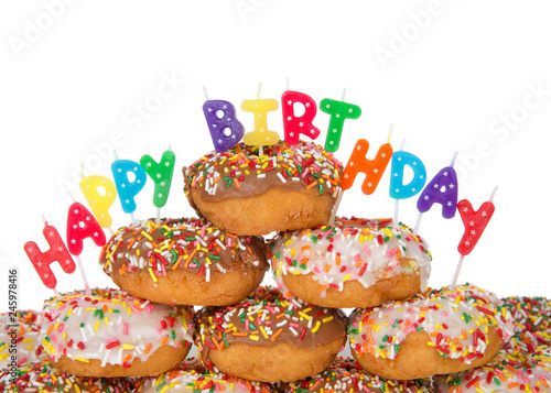 Chocolate and white frosted donuts covered in candy sprinkles piled into a cake pile isolated on white background with Happy Birthday candles.