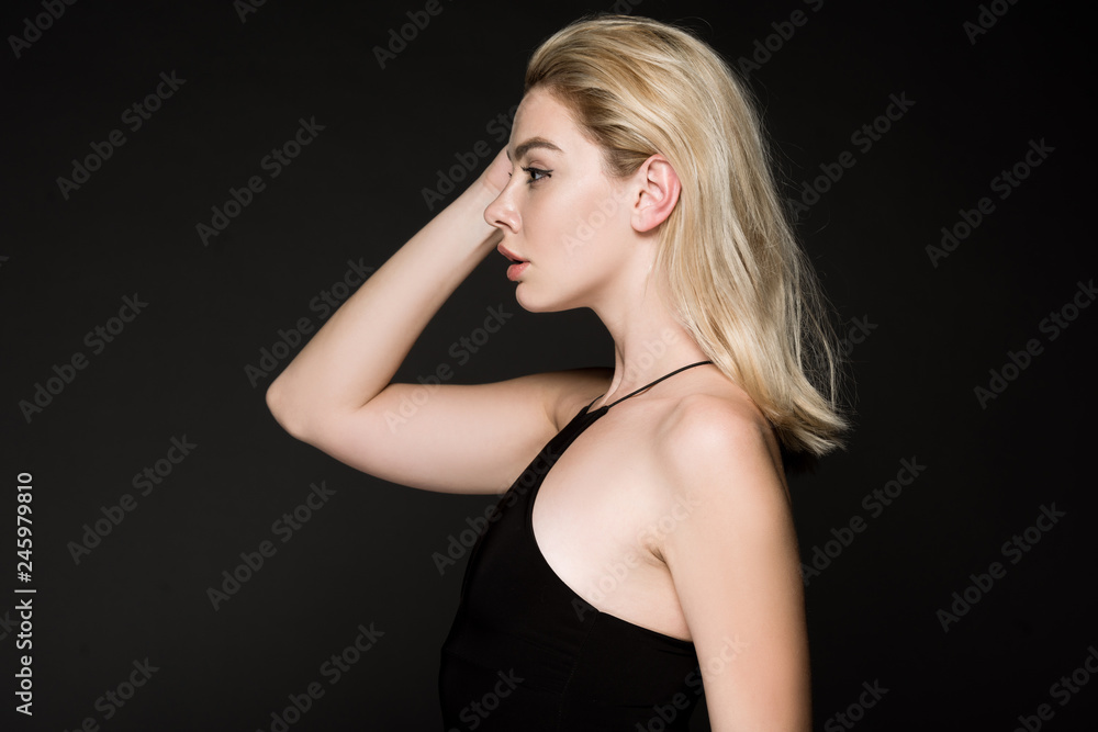 side view of blonde girl in black dress posing isolated on black