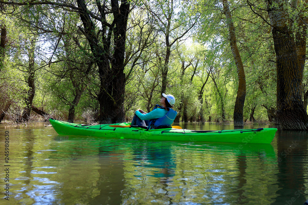 Girl in green kayak among flooded trees. Kayaking in wilderness areas at Danube river among flooded trees at spring high water on Danube biosphere reserve. Girl in green kayak among flooded trees. Kayaking in wilderness areas at Danube river among flooded trees at spring high water on Danube biosphere reserve.
