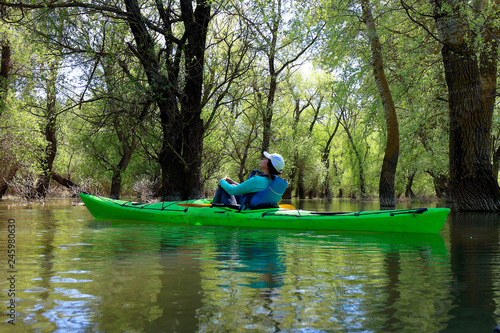 Girl in green kayak among flooded trees. Kayaking in wilderness areas at Danube river among flooded trees at spring high water on Danube biosphere reserve.