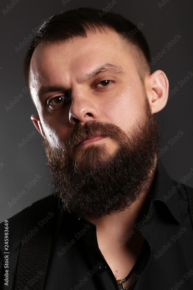 Obraz premium young handsome man with big beard in black t shirt on black background 