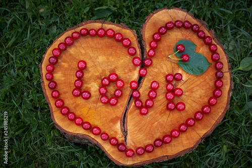 The heart and the word "love" are laid out with cherries on a cut wooden stump with a crack. Happy Valentine's Day. love concept. Summer sends love. Particles of art.