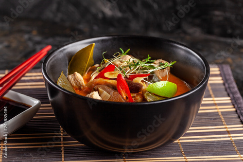 Concept of Asian cuisine. Thai soup Tom yam of chicken broth and coconut milk, mushrooms, chicken, chilli peppers, and vegetables. Japanese dish in black. Top view, copy space