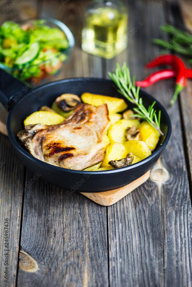 grilled pork steak with bone with potatoes and mushrooms in a frying pan on a wooden board grilled pork steak with bone with potatoes and mushrooms in a frying pan on a wooden board