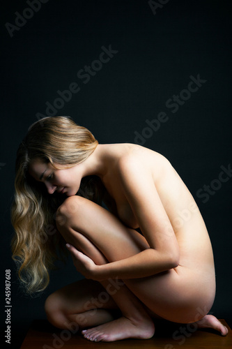 Side view of blond naked young woman sitting indoors
