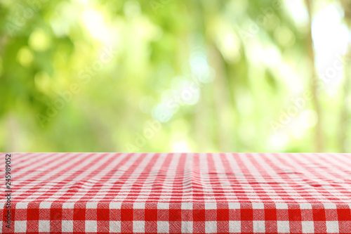Empty table with checkered red napkin on green blurred background. Space for design